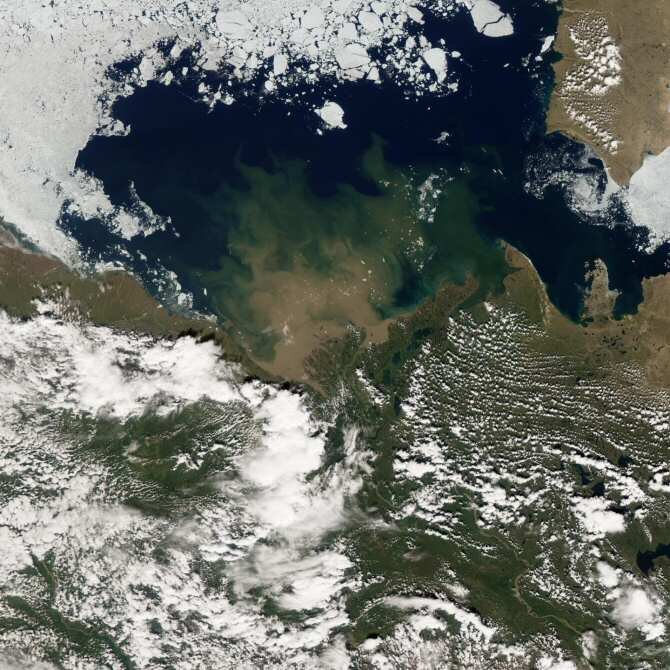 El agua del río Mackenzie, en Canadá, entrando en julio de 2012 en el océano Ártico, visible de color azul. Las zonas blancas en la mitad superior de la foto son en gran parte hielo marino, mientras que las de abajo son nubes sobre la tierra. (Foto:…